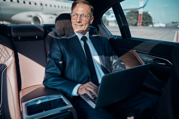Cheerful businessman with laptop in car at airport